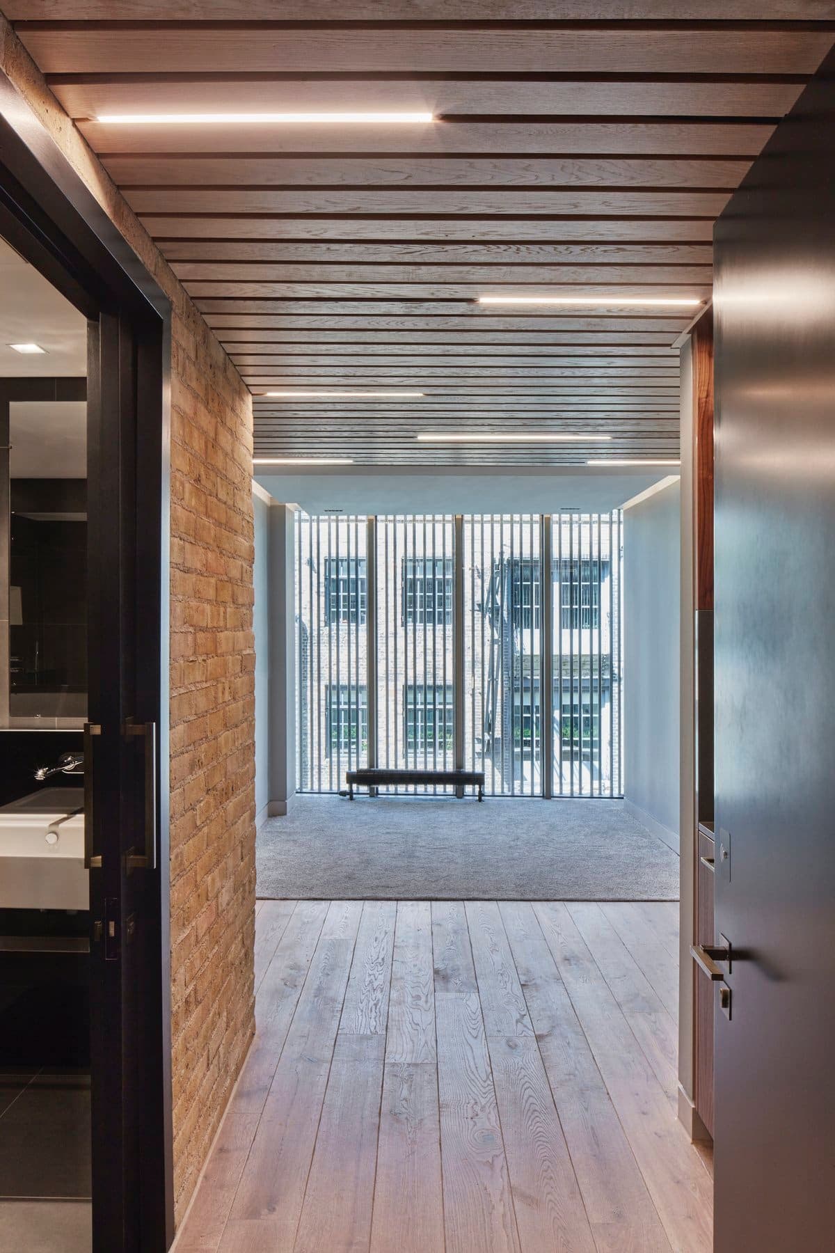 Modern minimalist hallway with wooden floors, exposed brick, and floor-to-ceiling windows.
