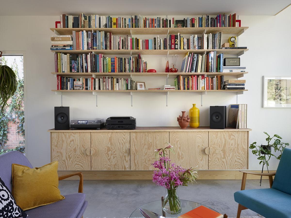 Modern living room with vibrant accents, featuring a bookshelf, stylish seating, and floral decor.