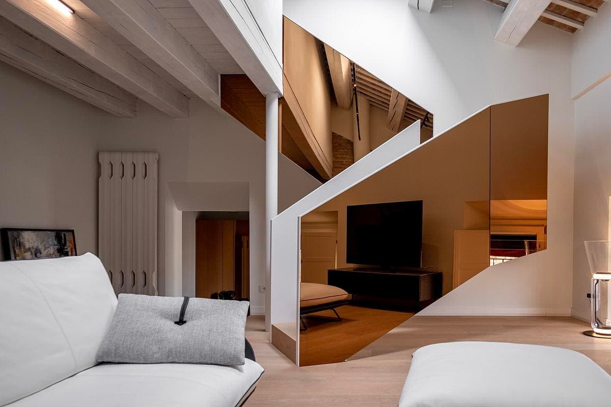 Modern minimalist living space with a white sofa, warm wood flooring, and striking triangular mirror panel.