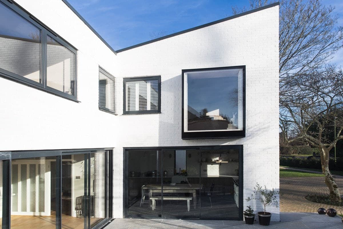 Modern minimalist white two-story house with large black-framed windows and a well-maintained garden.