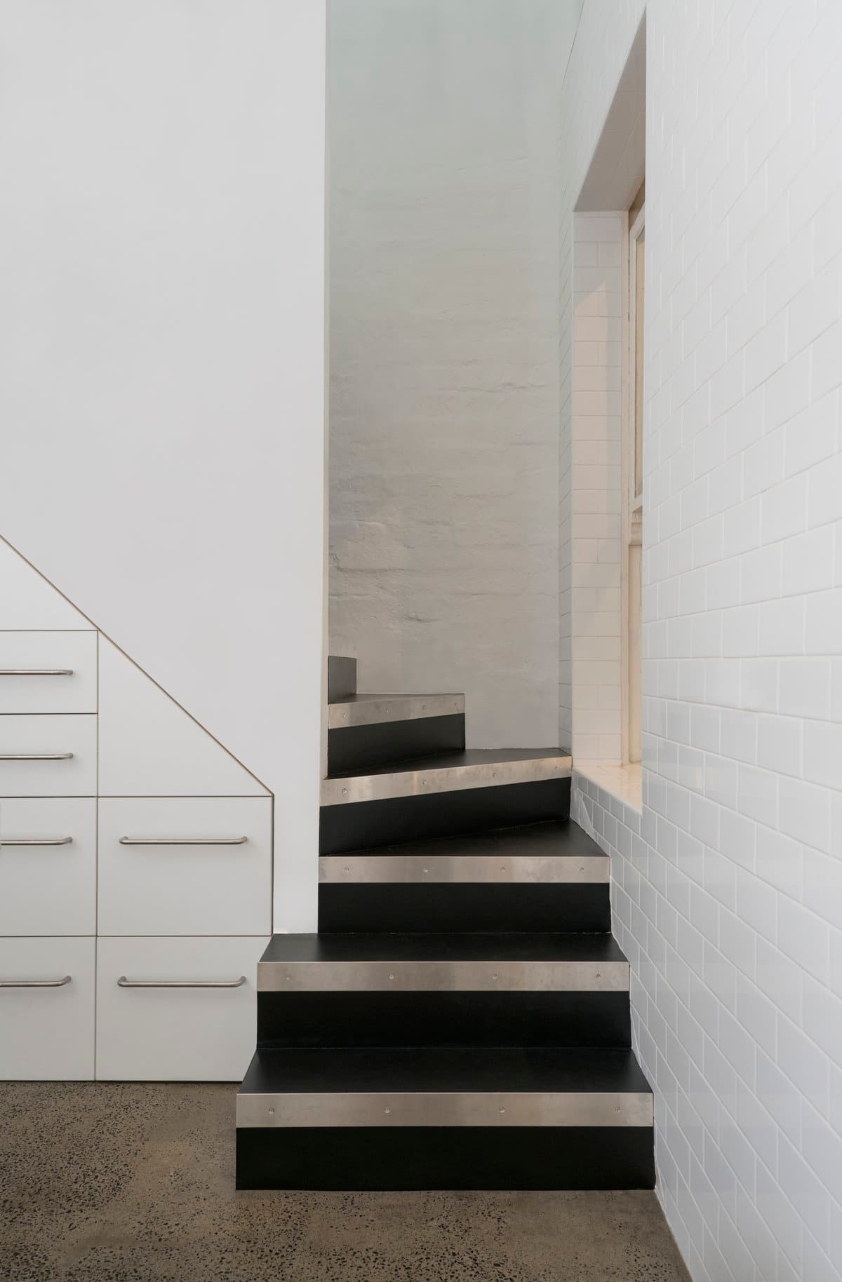 Minimalist dark-step modern staircase with built-in storage, white walls, and polished concrete flooring.
