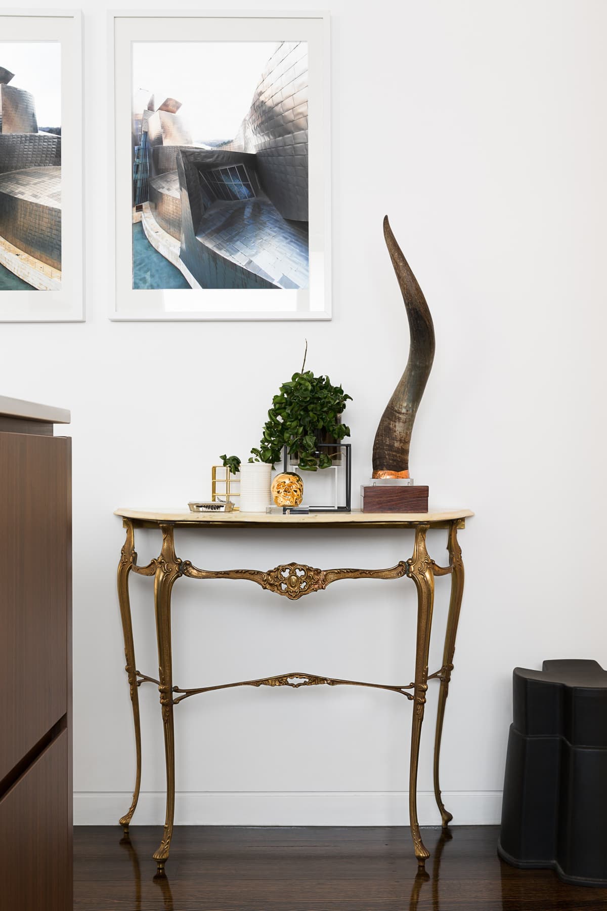 Minimalist interior with decorative gold table, abstract wall art, and elegant plant arrangement.