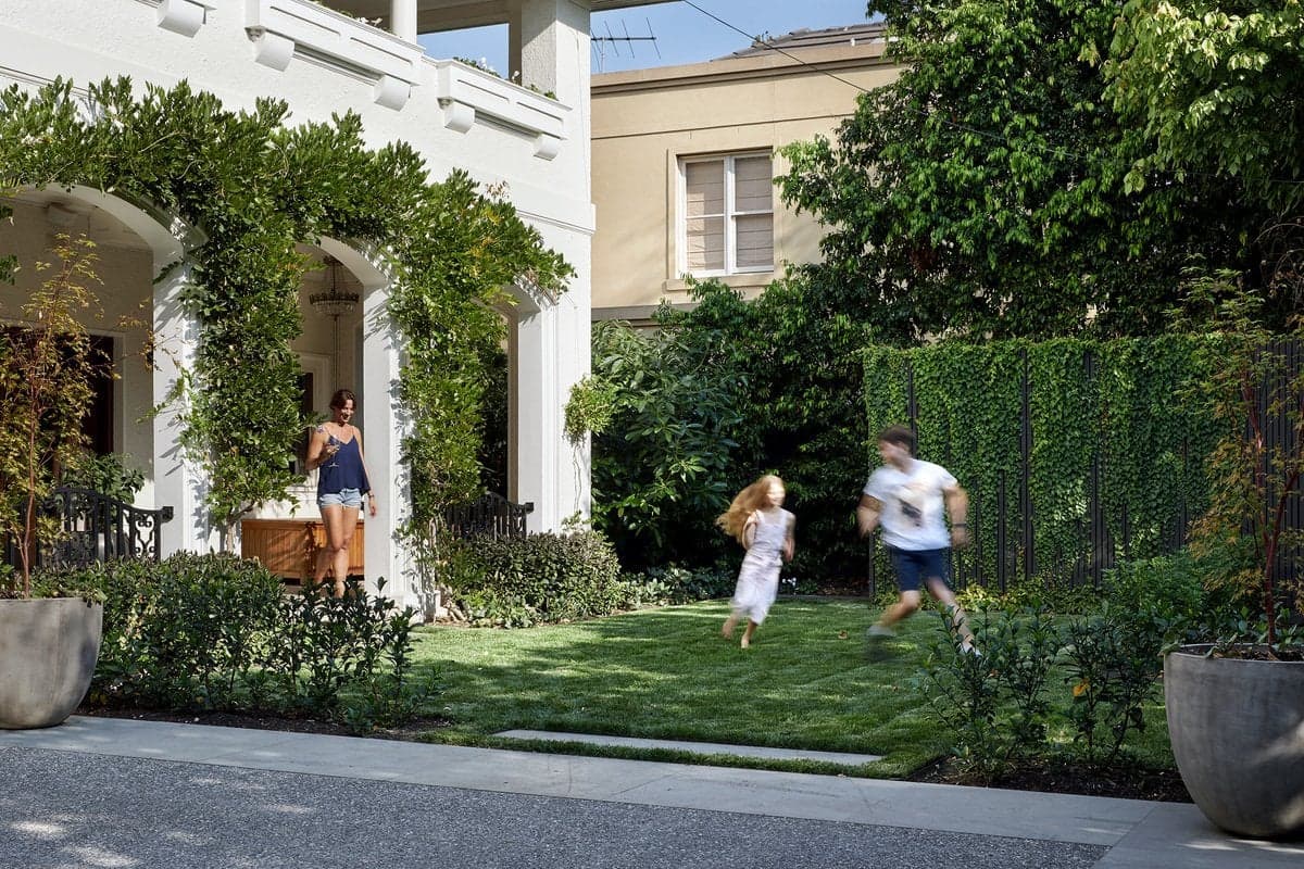 Family enjoying garden playtime on a sunny day, with greenery and a classic white house backdrop.