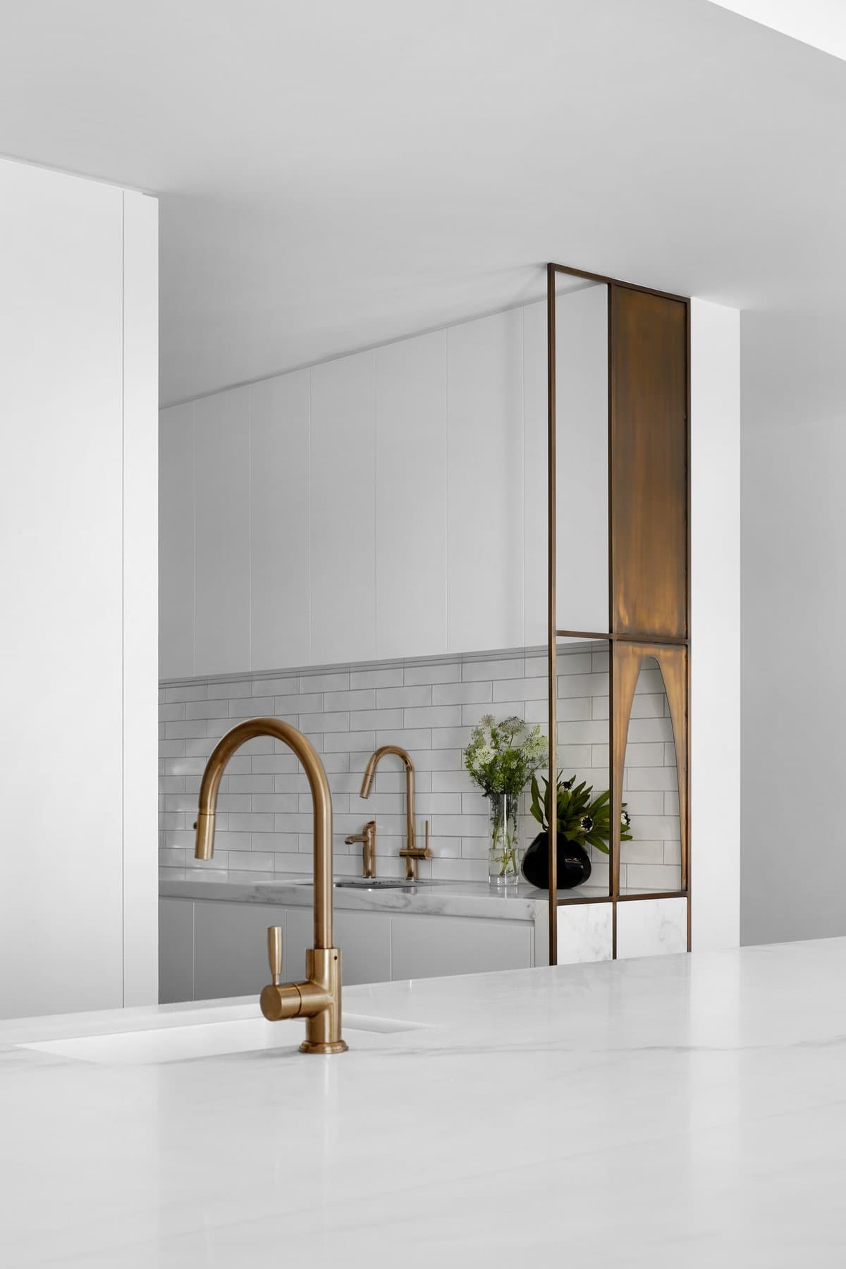Minimalist kitchen with gold fixtures, white countertop, subway tile backsplash, and glass partition.