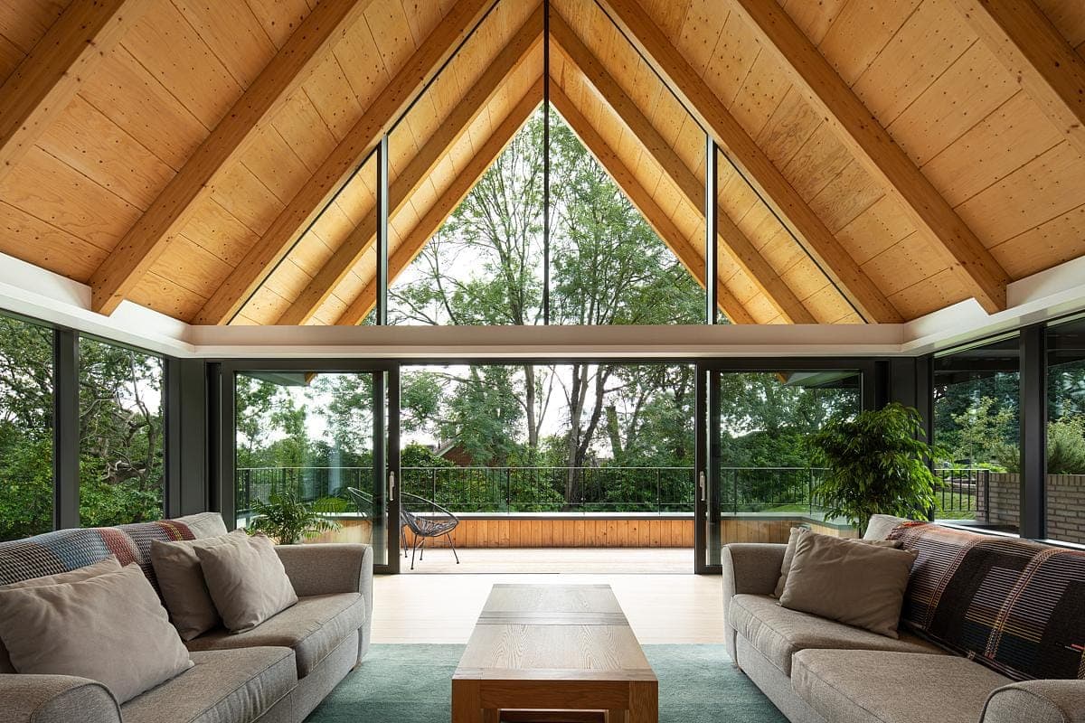 Contemporary living room featuring a high wooden ceiling and large windows connecting indoors with nature.