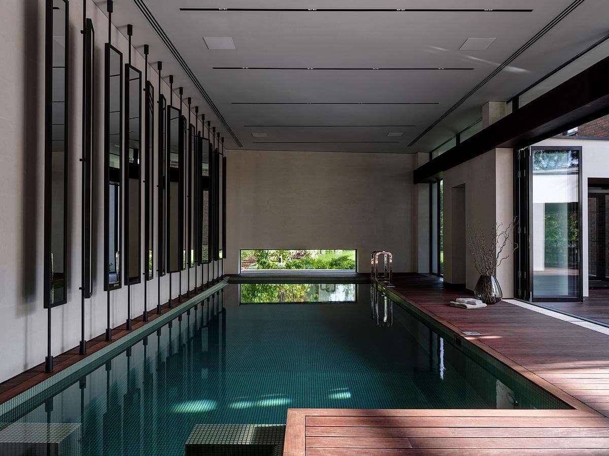 Elegant indoor swimming pool with large windows, wooden decking, and serene natural light.