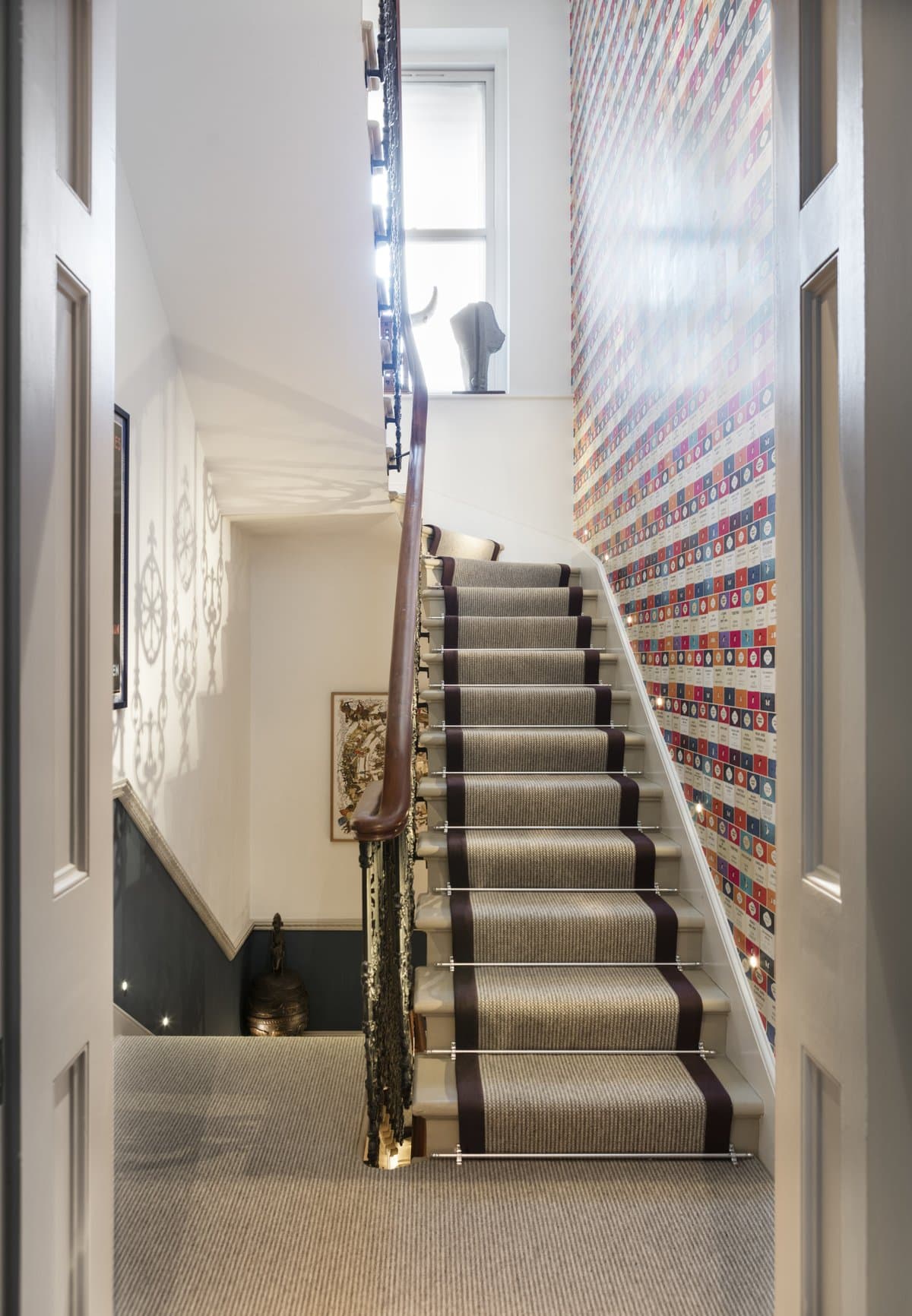 Stylish interior staircase with carpet runner, wooden handrail, artwork, and vibrant wallpaper.