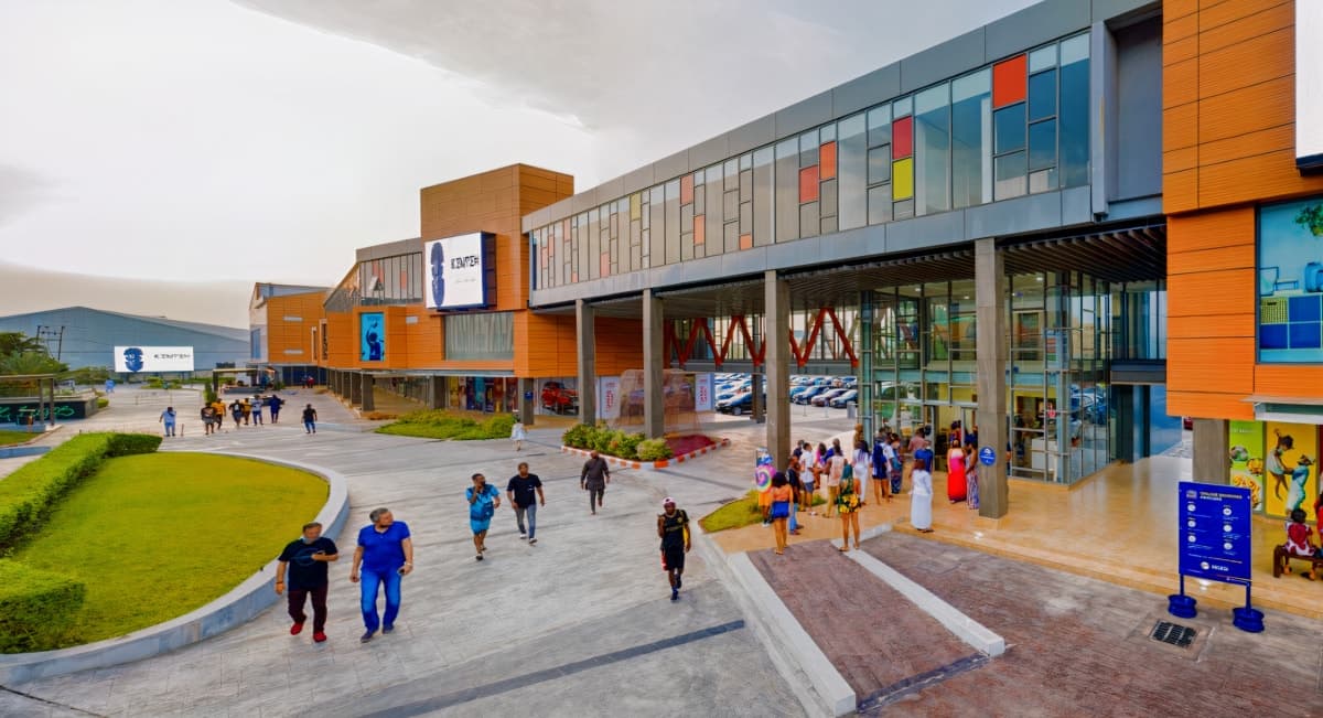 Modern retail complex with glass facade, colourful panels, and bustling entrance.