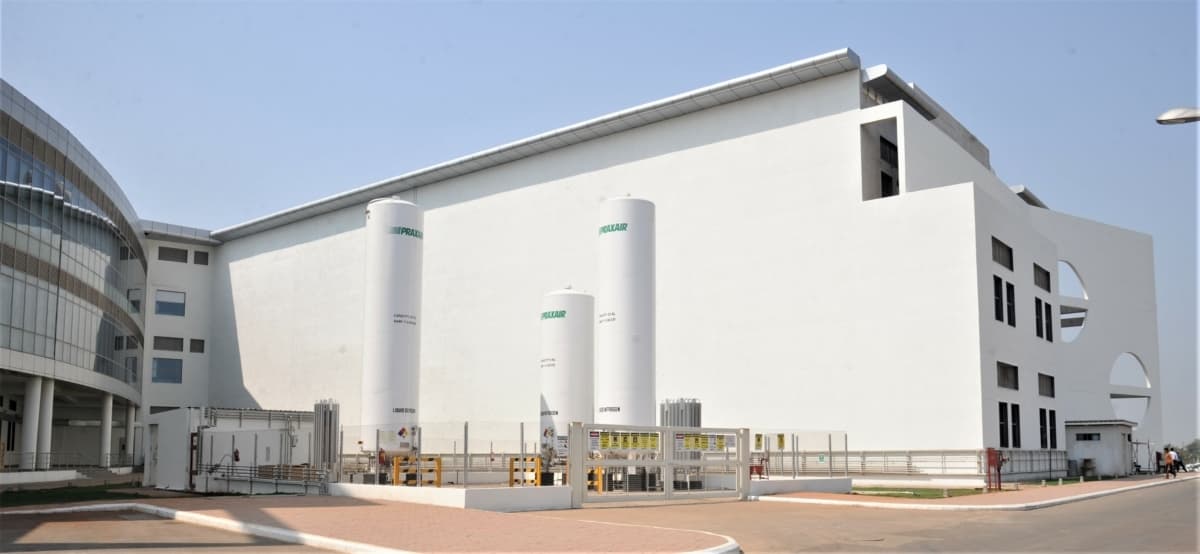 Modern industrial facility with white building, cylindrical tanks, curved glass entrance, and paved area.