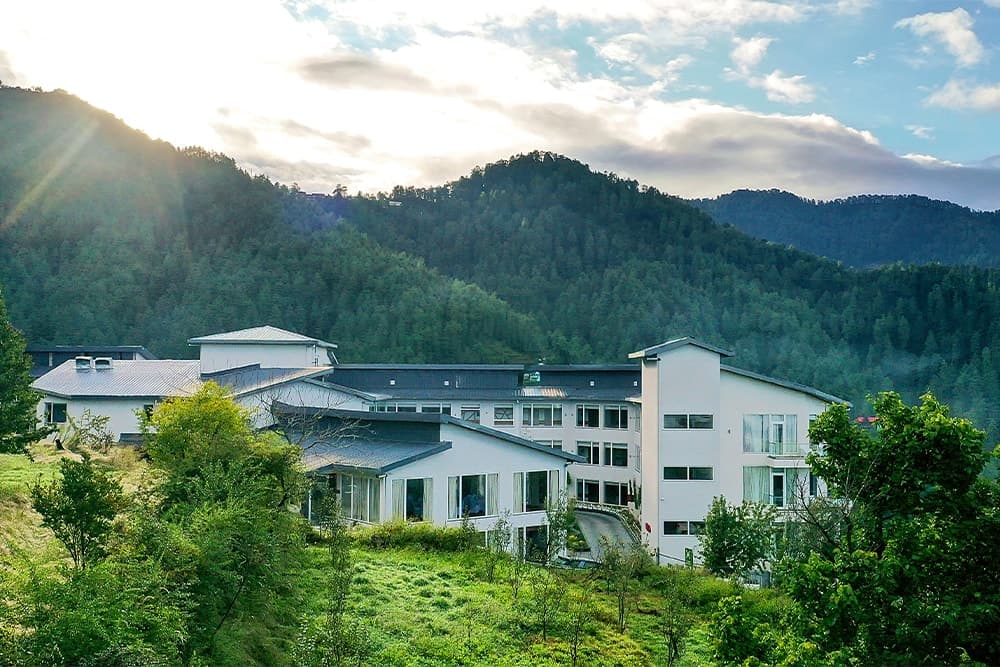 Modern white hotel nestled in lush mountains with scenic views and serene greenery.