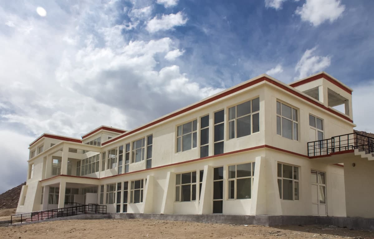 Modern two-story building at Leh Satellite Campus, Kashmir University, against a partly cloudy sky.