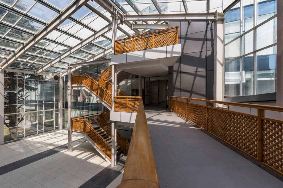 Modern atrium with glass ceiling, wooden walkway, and central glass-enclosed staircase at Kashmir University.