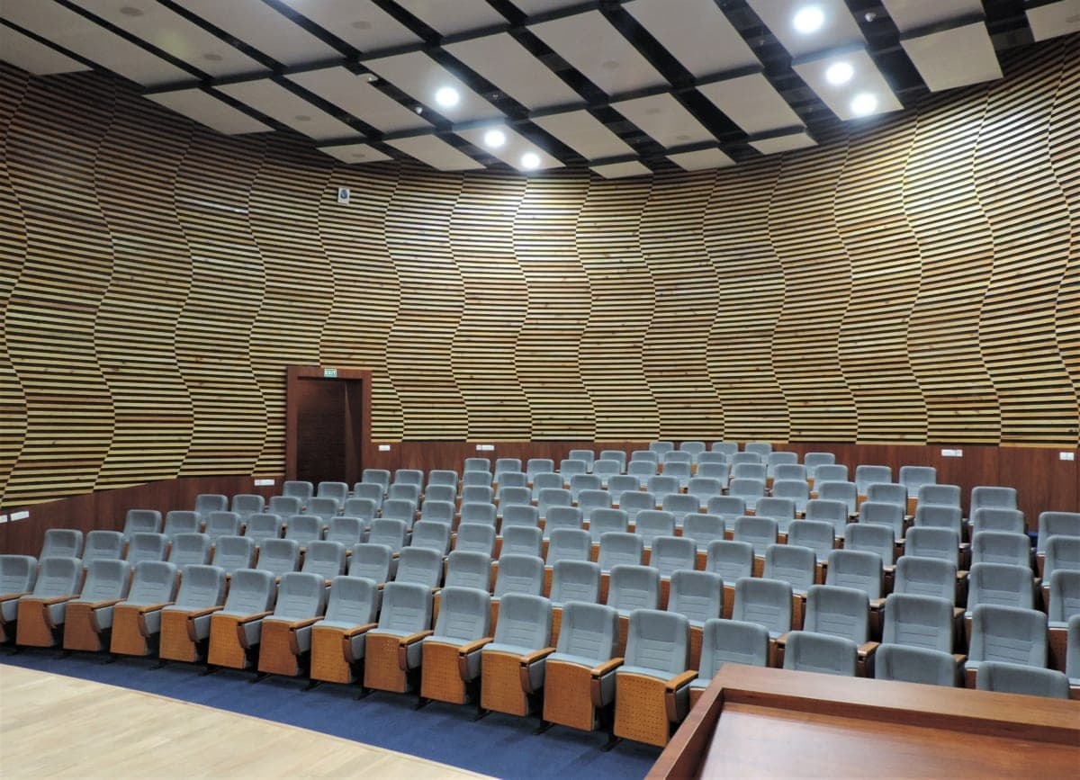 Modern auditorium with cushioned seating, wood paneling, and recessed lighting at Reliance Technology Group.