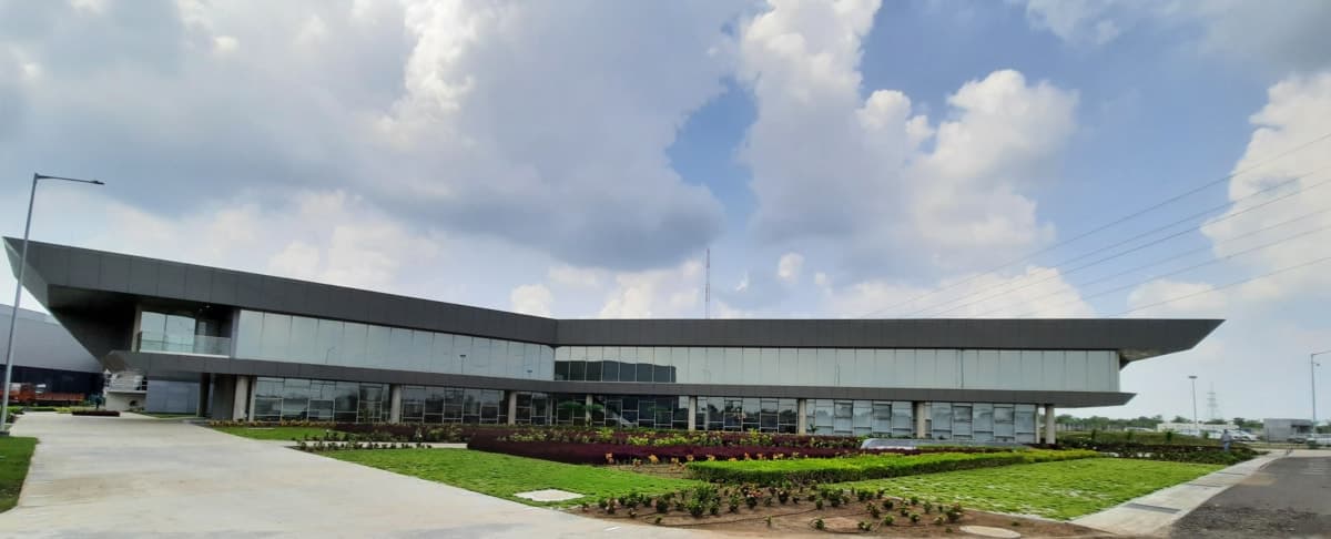 Modern, sleek building with glass facade, overhanging roof, landscaped garden, and clear blue sky.
