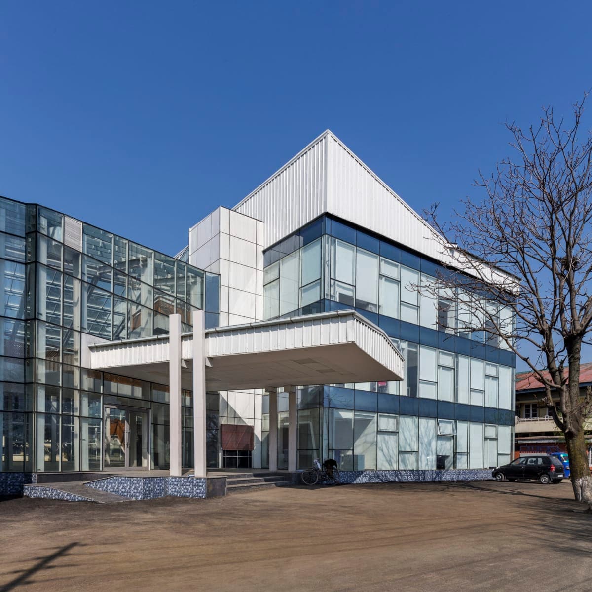 Modern glass and concrete university administration building with canopy entrance and paved pedestrian area.
