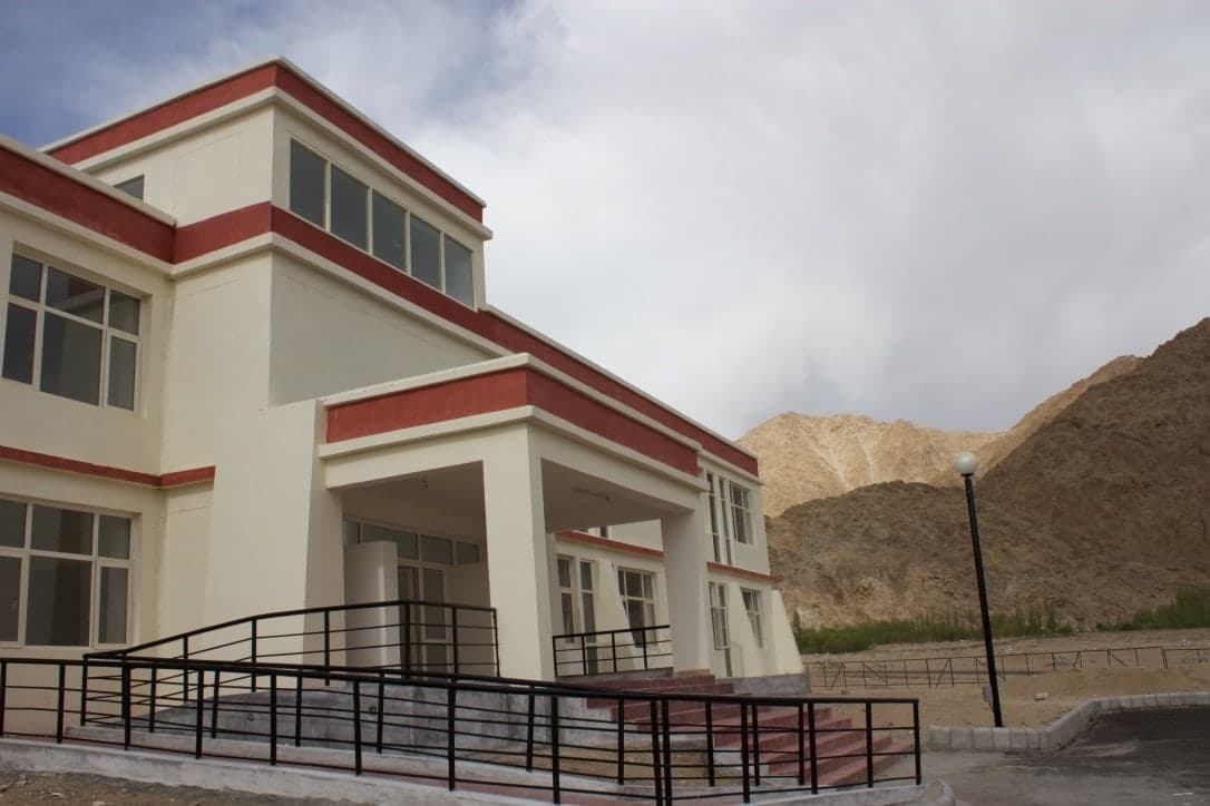 Modern multi-story building with large windows and ramps, against a mountainous backdrop.
