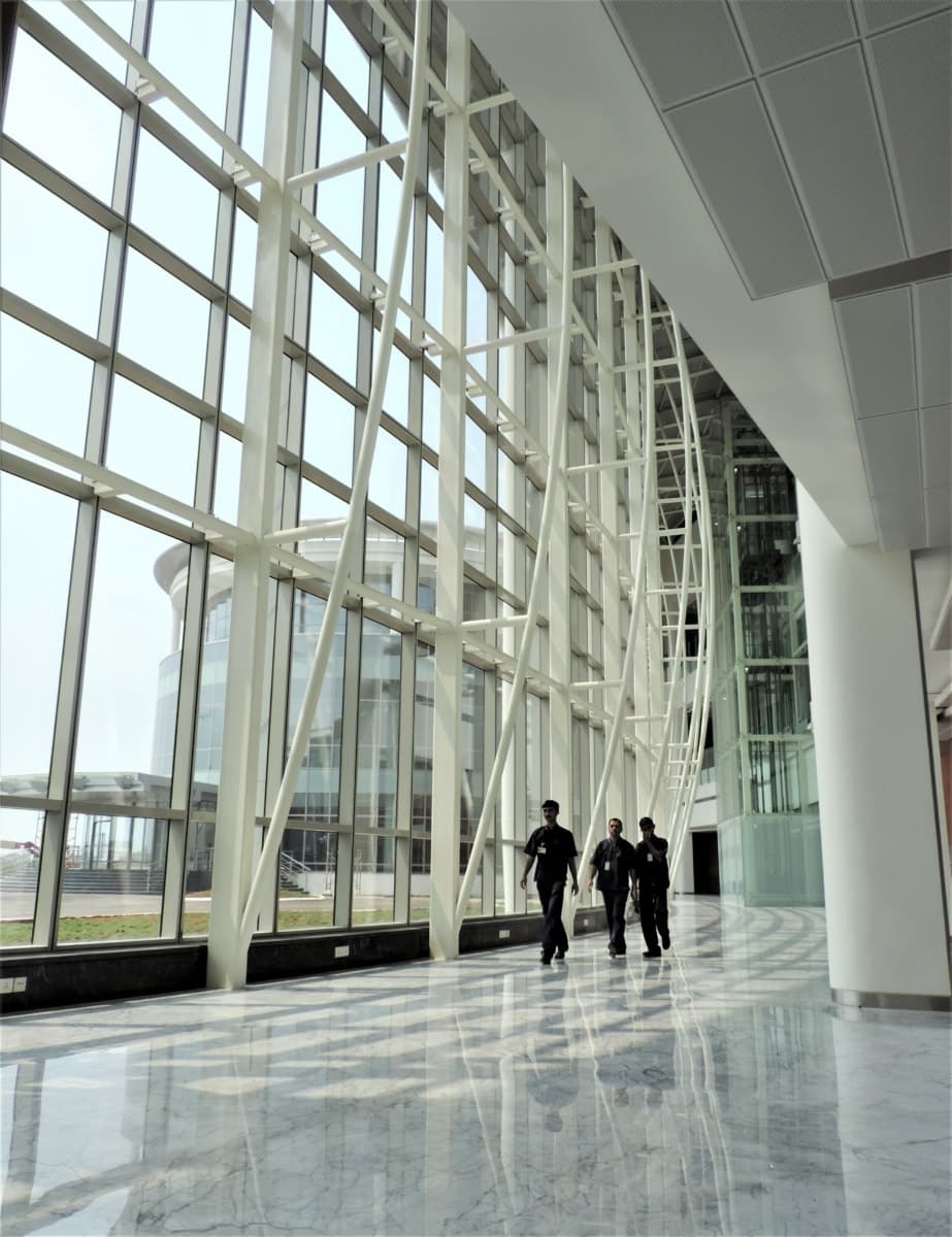 Modern glass-walled research facility with marble floors, metal beams, and people walking inside.
