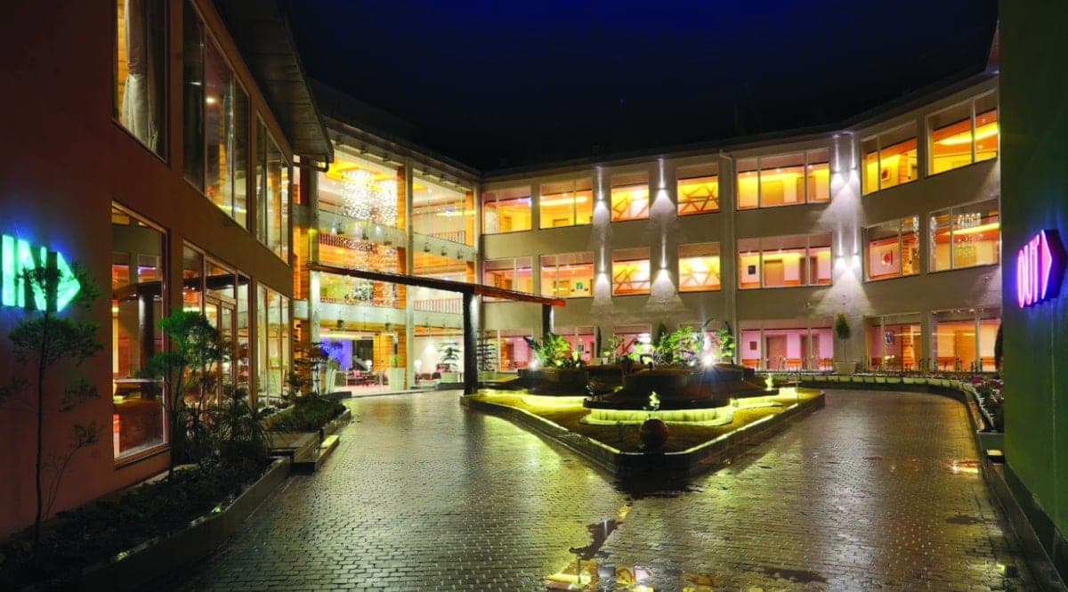 Modern hotel at night with large windows, landscaped courtyard, and vibrant neon lights.