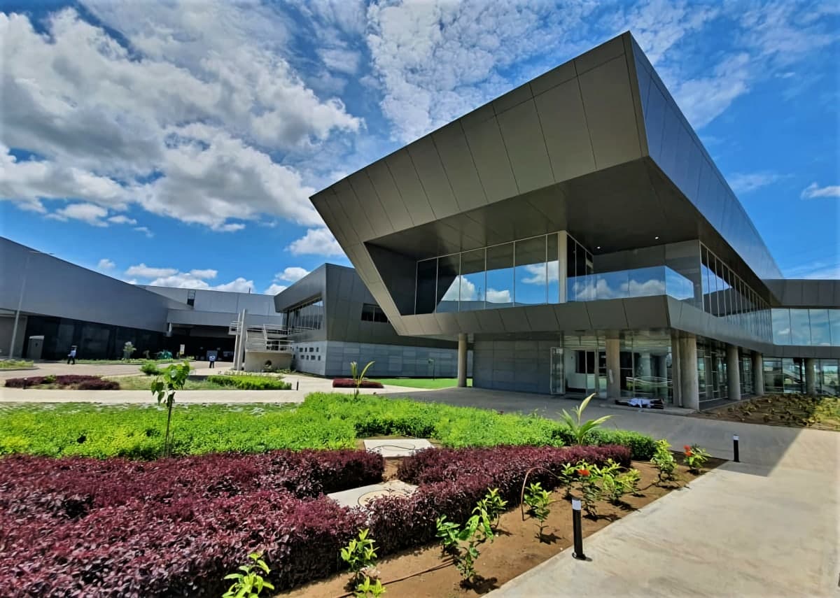 Modern Plasser India building with geometric design and landscaped garden under a bright blue sky.