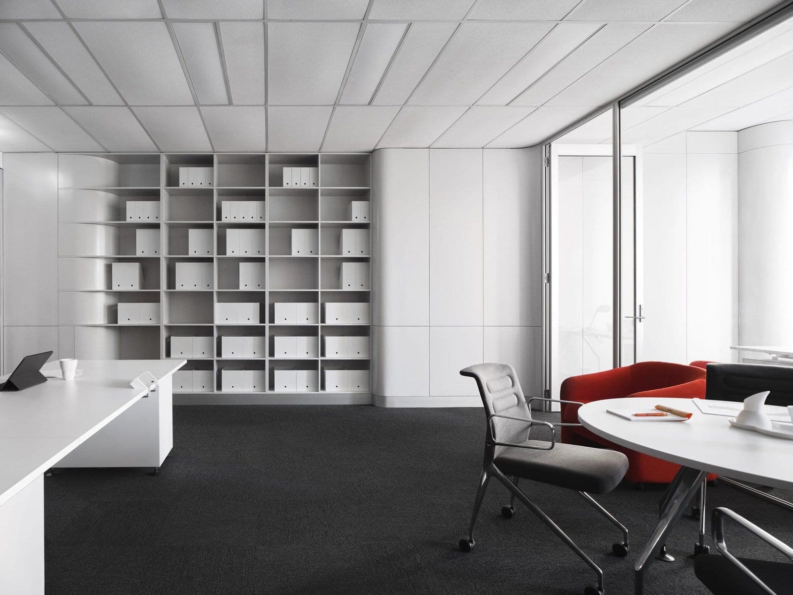Minimalist modern office with white furniture, red couch, natural light, and organised shelving.