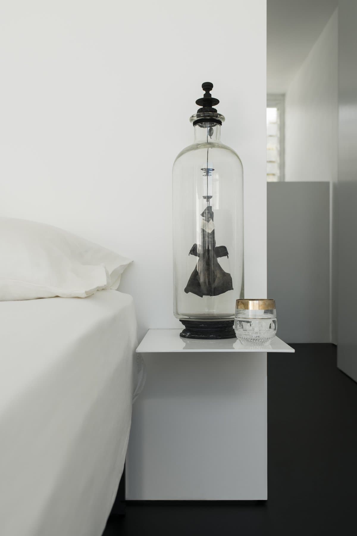 Minimalist bedroom corner with white bedside table, glass dome, and elegant decor.