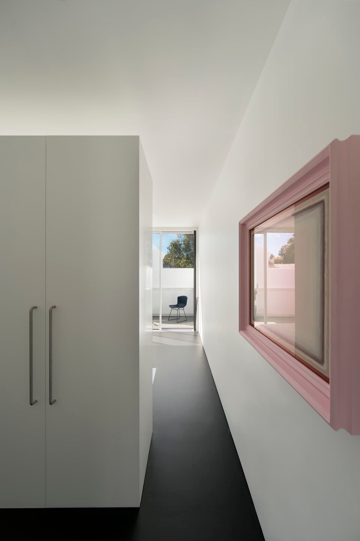 Modern minimalist corridor with white walls, pastel pink window frame, and natural light.