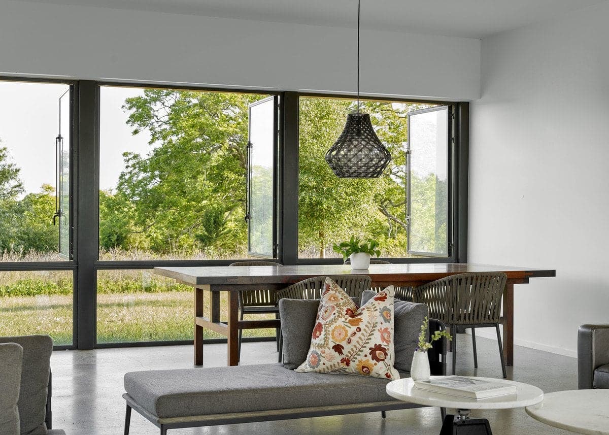 Modern open-concept living-dining area with gray sofa, wooden dining table, and floor-to-ceiling windows.