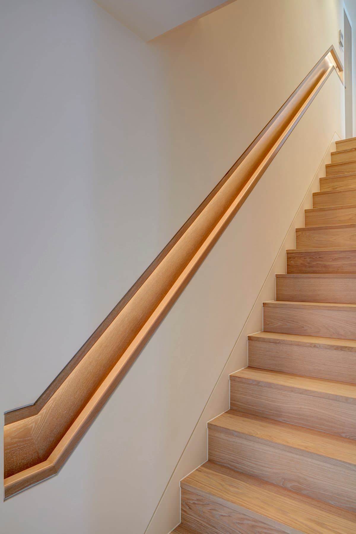 Modern minimalist staircase with light wood, recessed handrail, and integrated lighting.