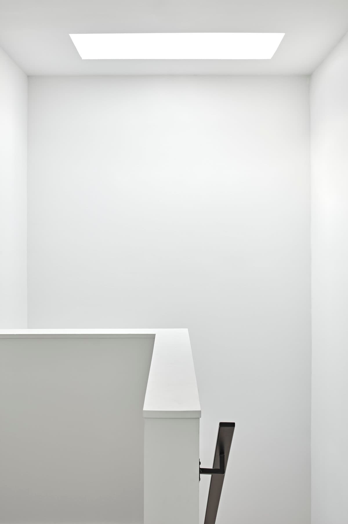 Minimalistic white interior with skylight, staircase railing, and dark handrail contrast.