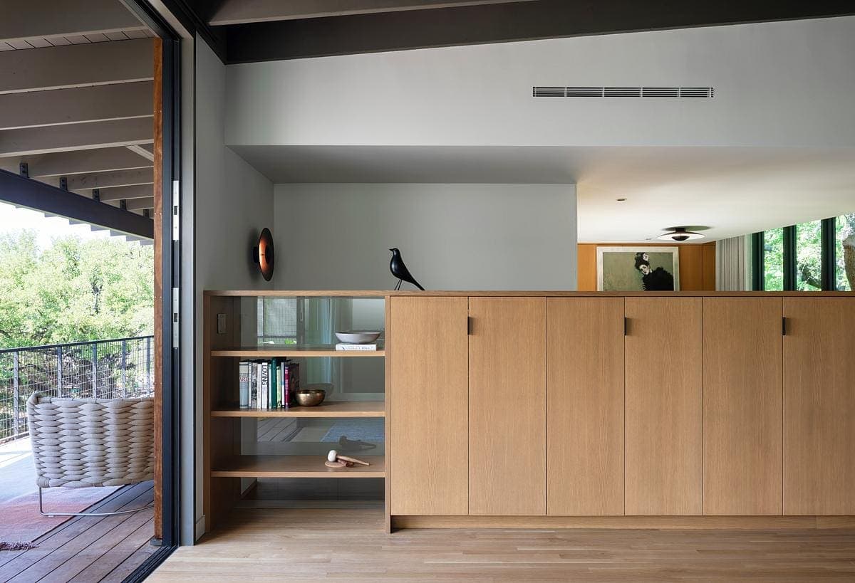 Modern minimalist living room with natural light, wooden accents, and views of lush greenery.