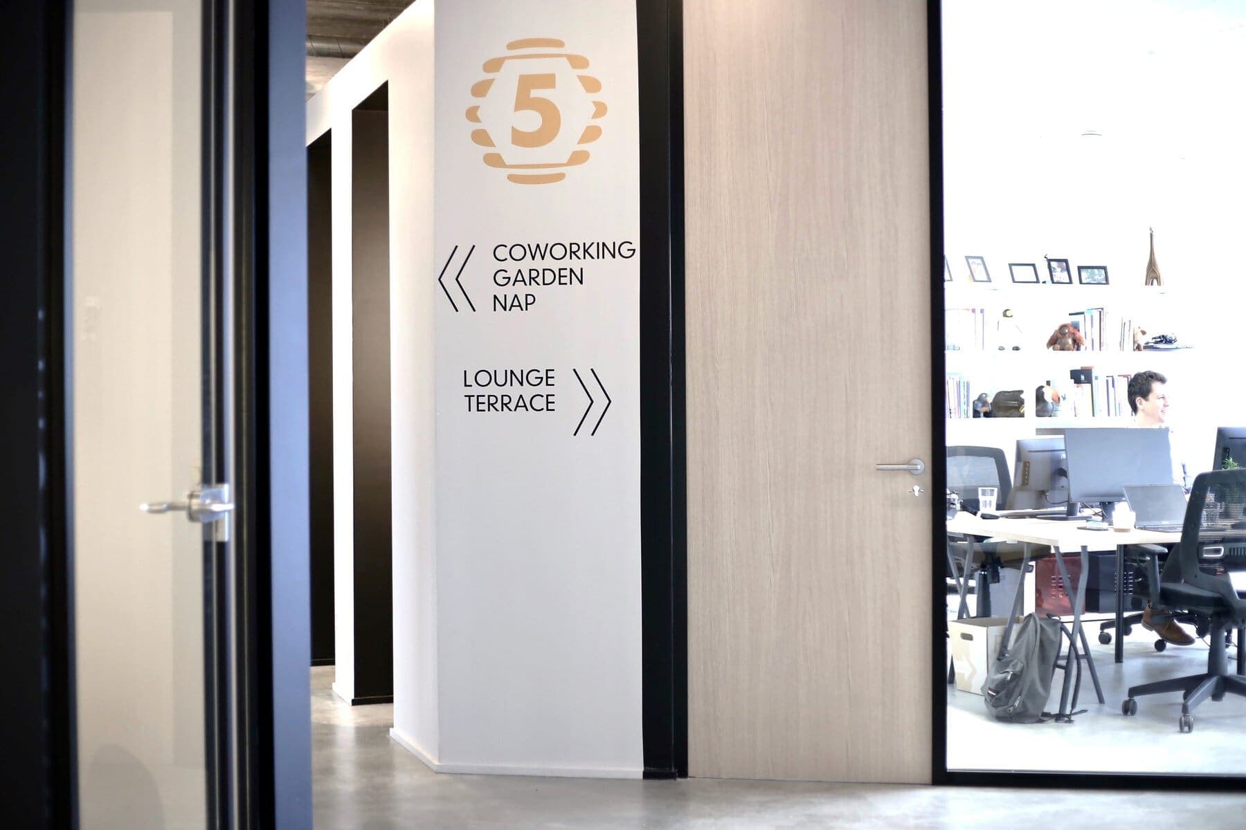Modern minimalist office interior with open hallway, clear signage, and glass-partitioned workstations.