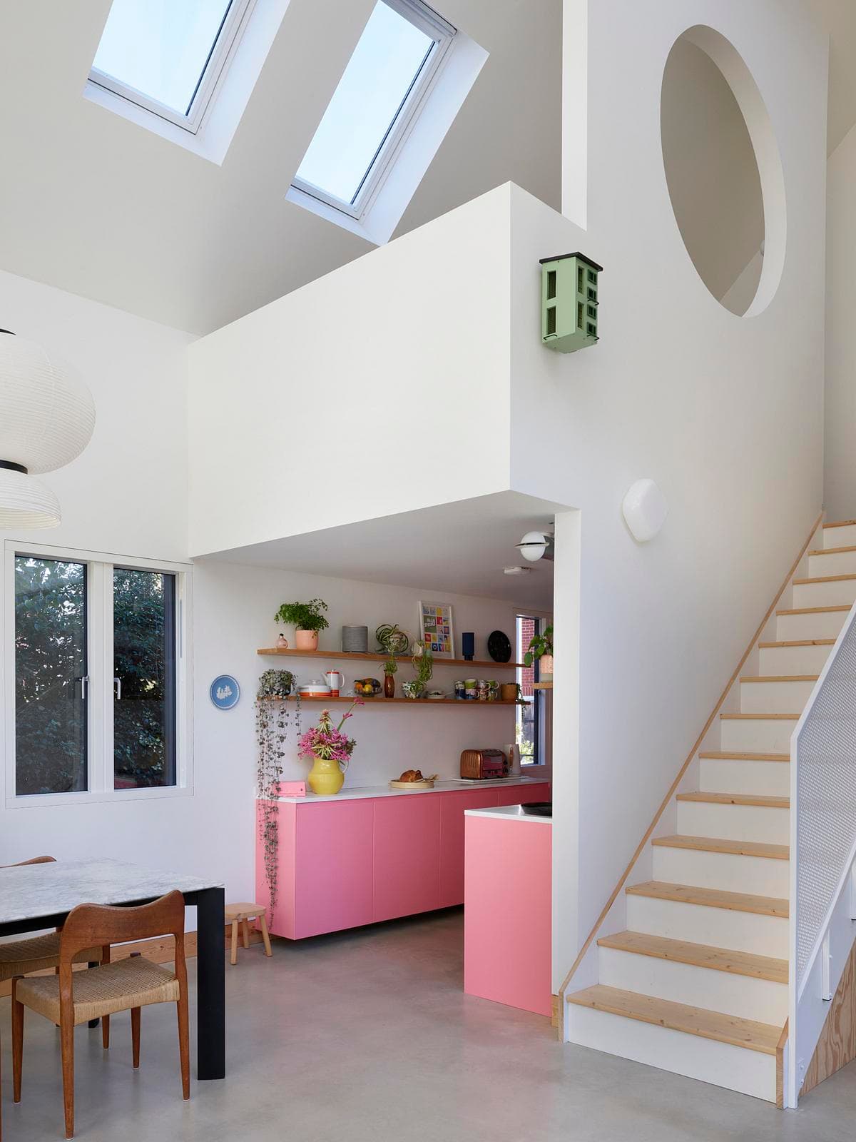 Modern minimalist kitchen with vibrant pink island and open living space design.