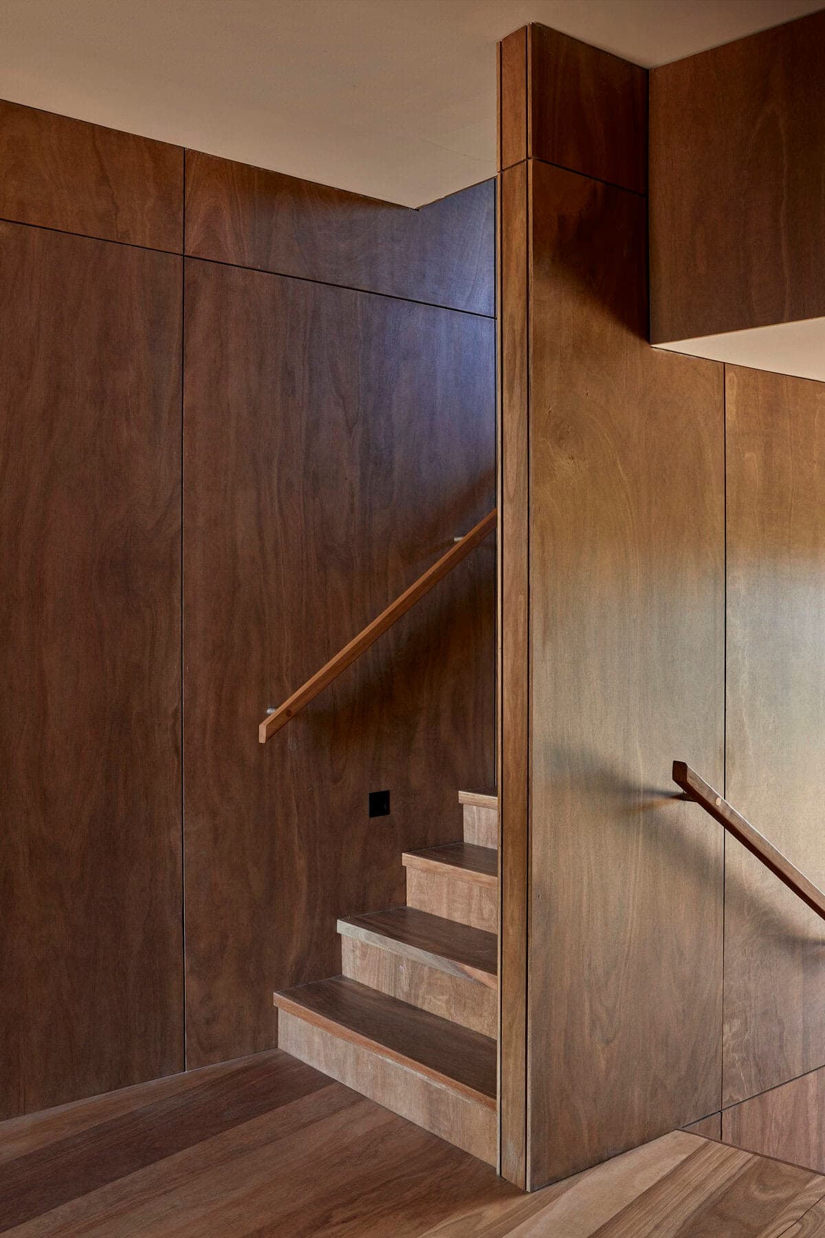 Stylish minimalist wooden staircase with elegant handrail and warm wooden paneling.