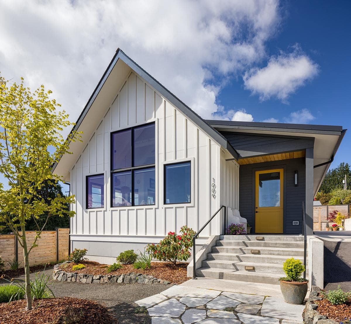 Modern A-frame house with striking colours and inviting entrance steps in a tranquil setting.