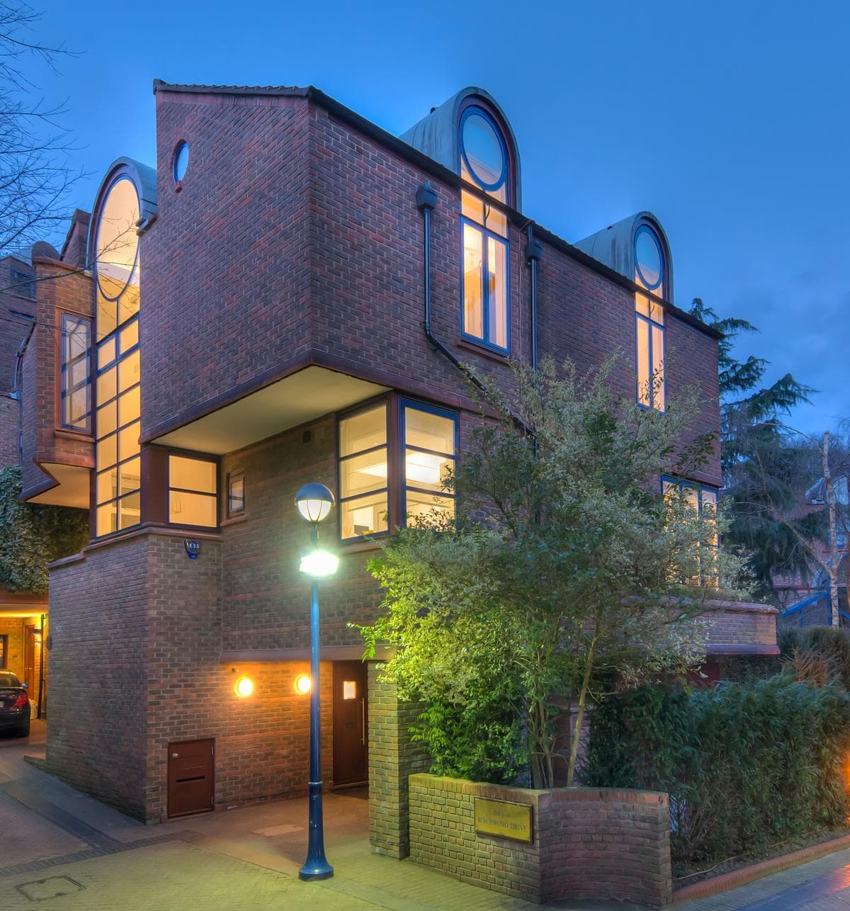 Stylish modern brick home glowing at dusk, surrounded by lush greenery and warm lighting.