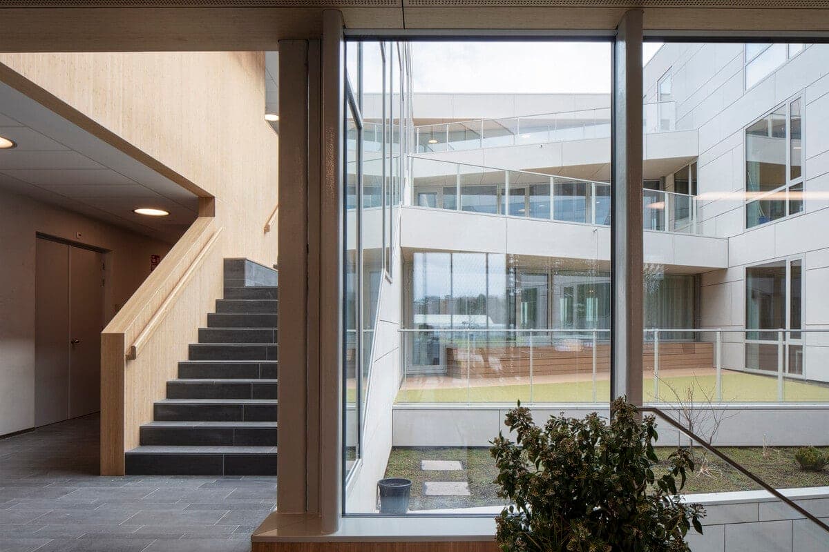 Minimalist modern healthcare clinic interior with large window view of courtyard, staircase, and plants.