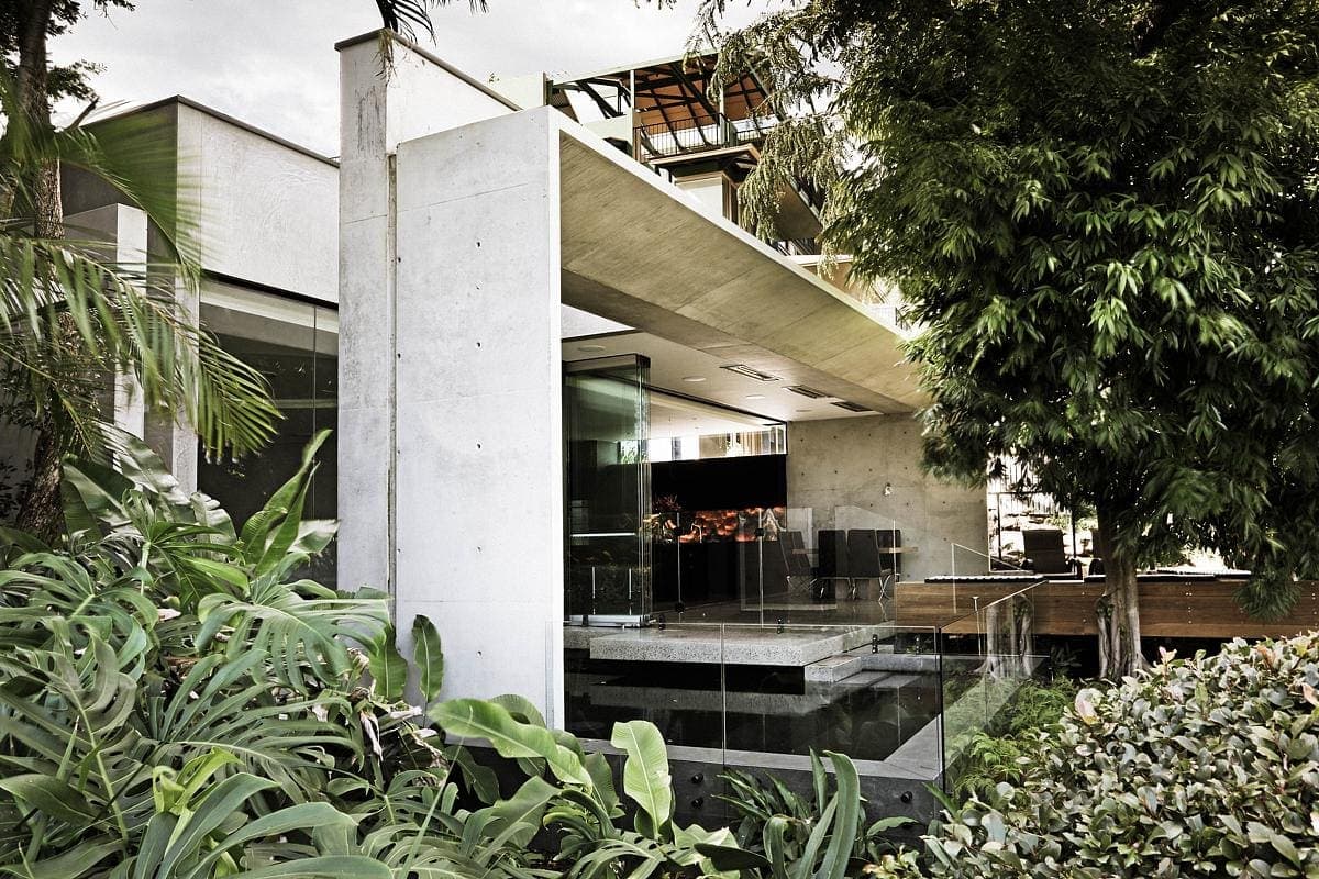 Modern minimalist concrete and glass building surrounded by lush greenery.