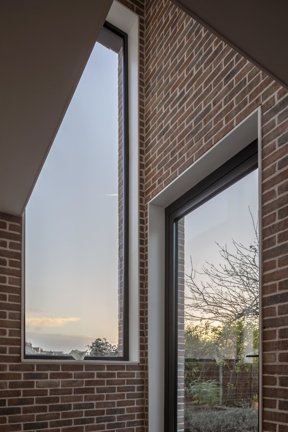 Modern room with angular windows, exposed brickwork, natural light, and an outdoor scenic view.