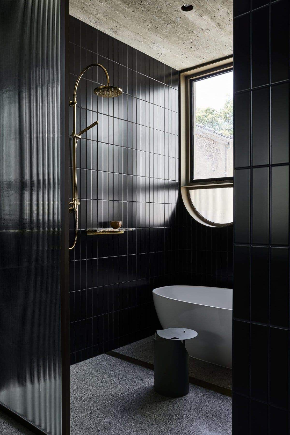 Contemporary bathroom with dark tiles, freestanding tub, and elegant gold fixtures.