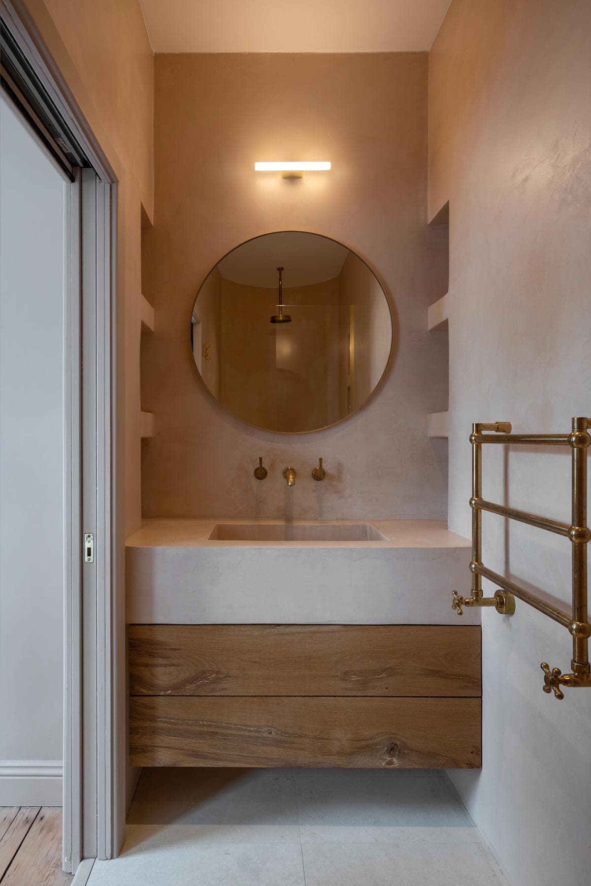 Chic modern bathroom featuring a round mirror, gold faucets, and minimalist design elements.