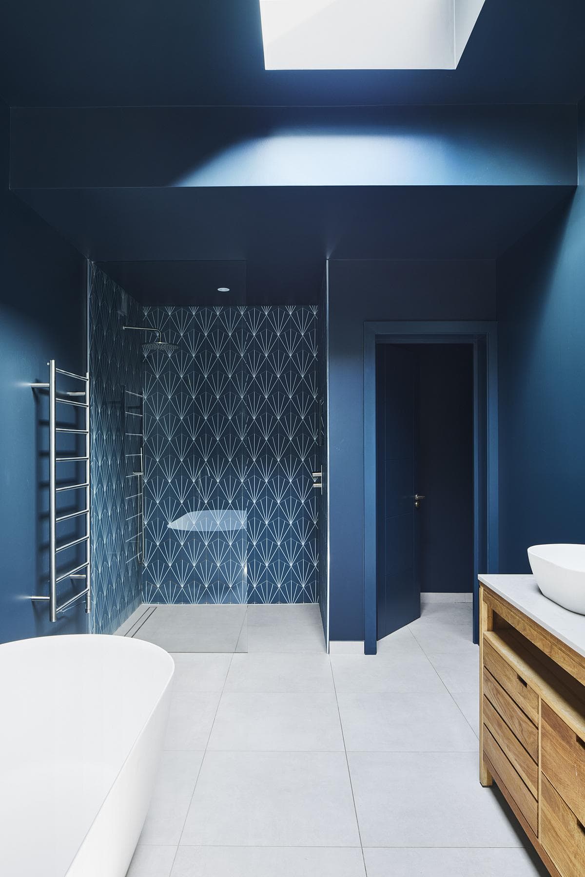 Sleek modern bathroom in deep blue tones with freestanding tub and stylish wooden vanity.