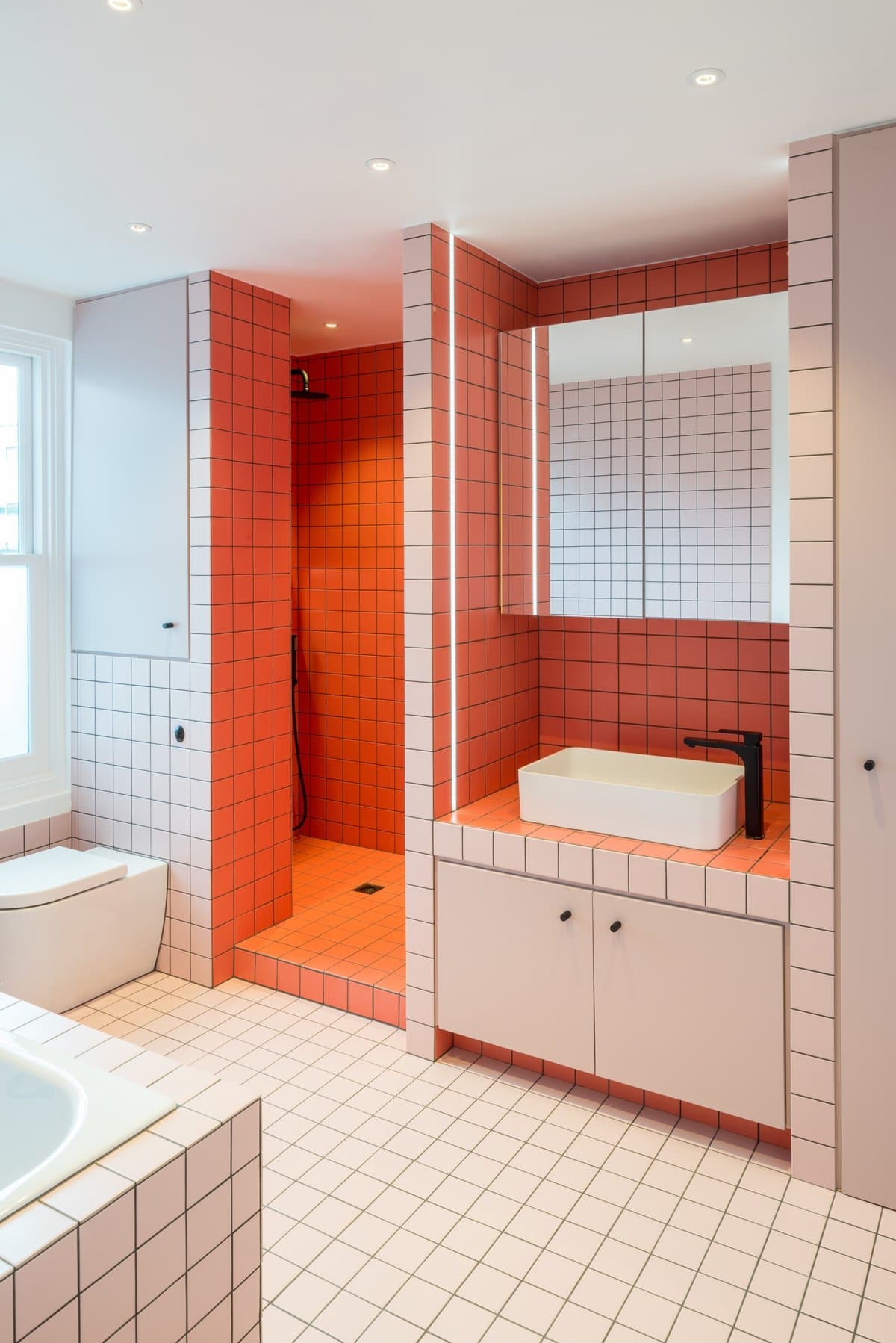 Modern bathroom with bold red tiles, white vanity, and natural light.