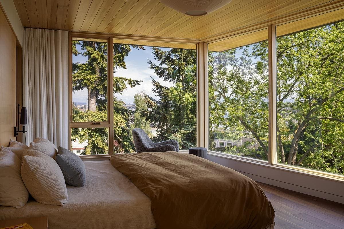 Modern bedroom with nature views, large windows, warm wood tones, and inviting decor for relaxation.
