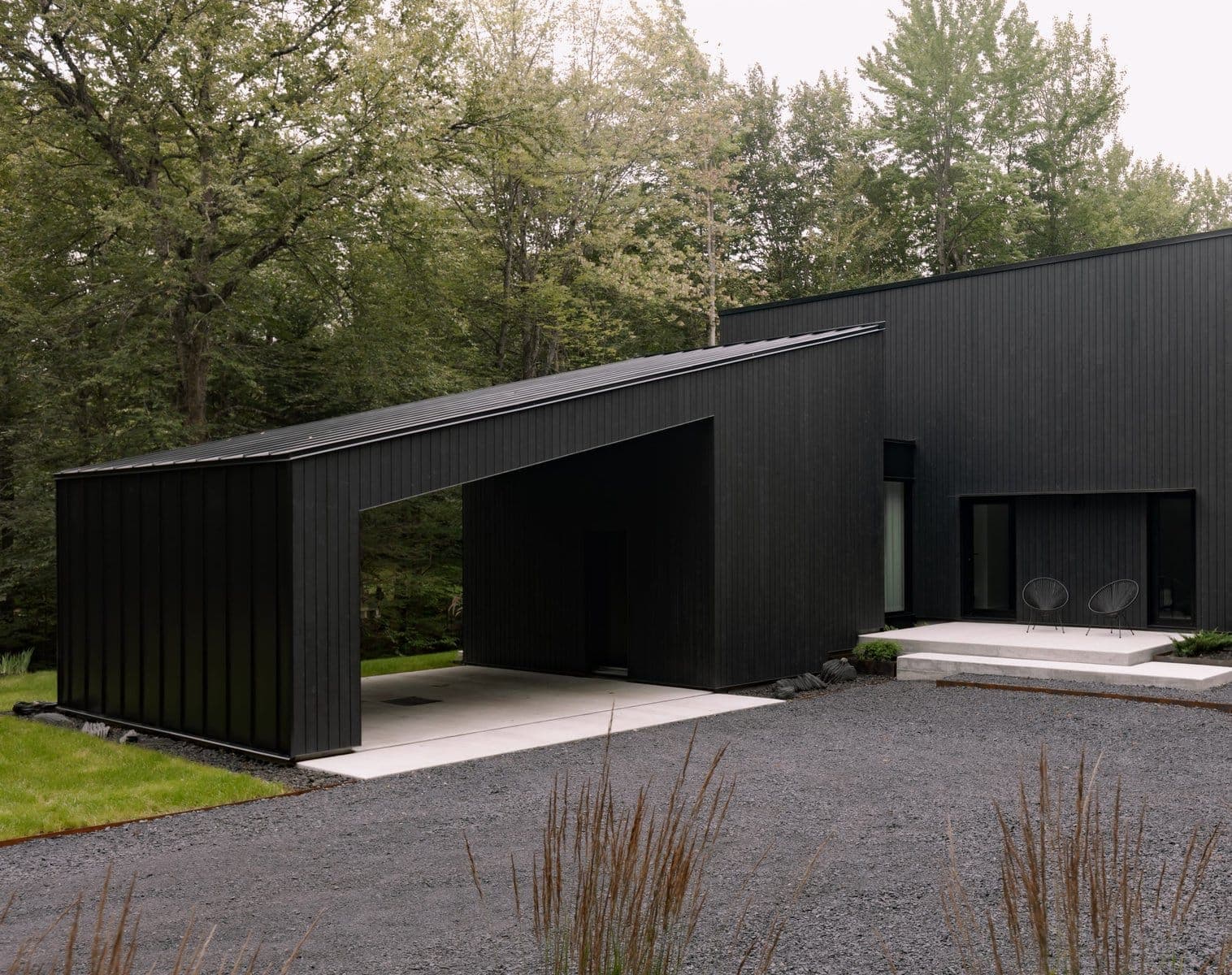 Contemporary black home in nature, featuring minimalist design, large windows and lush landscaping.
