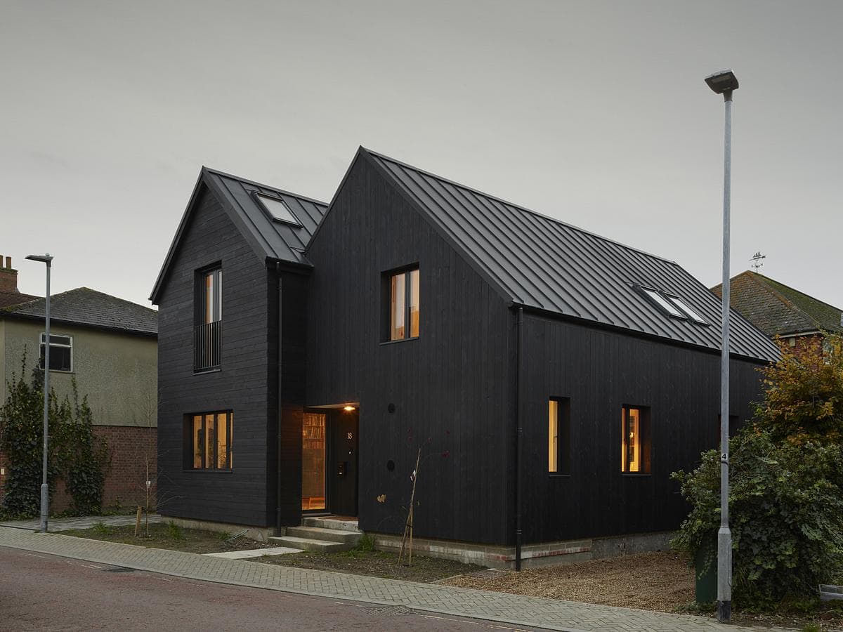 Bold modern black house with unique asymmetrical design and large windows in a minimalist landscape.