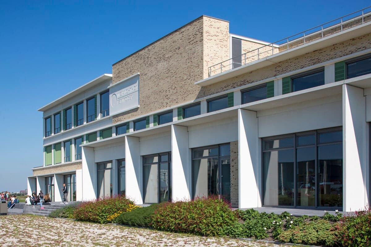 Modern two-story concrete and glass building with green panels and garden, clear sky.