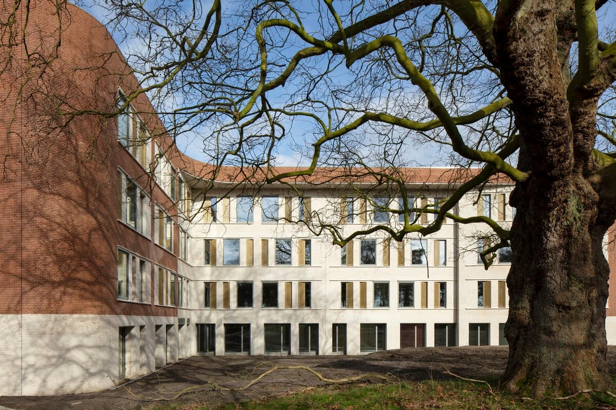 Modern healthcare clinic with red brick facade and large tree in foreground.