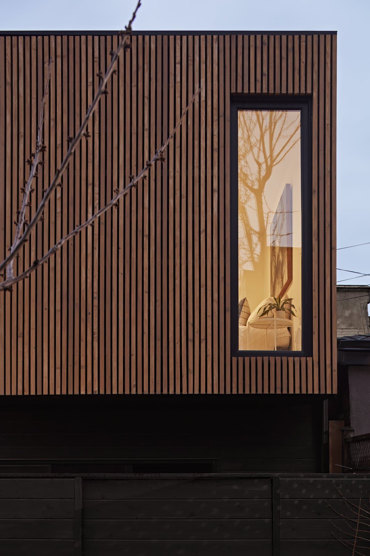 Modern building with vertical wooden slats and a tall window, part of an urban setting.
