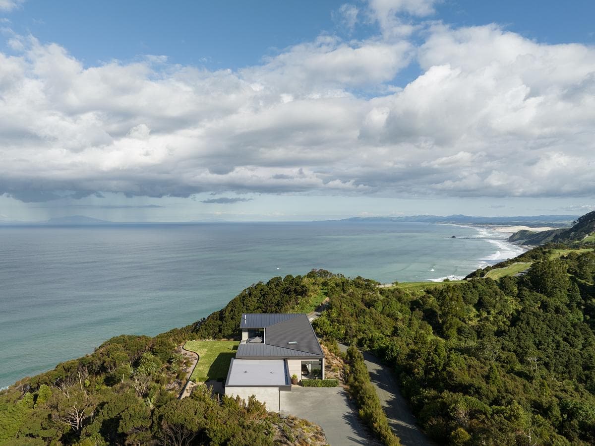 Aerial view of a modern coastal retreat with ocean views and lush hillside surroundings.