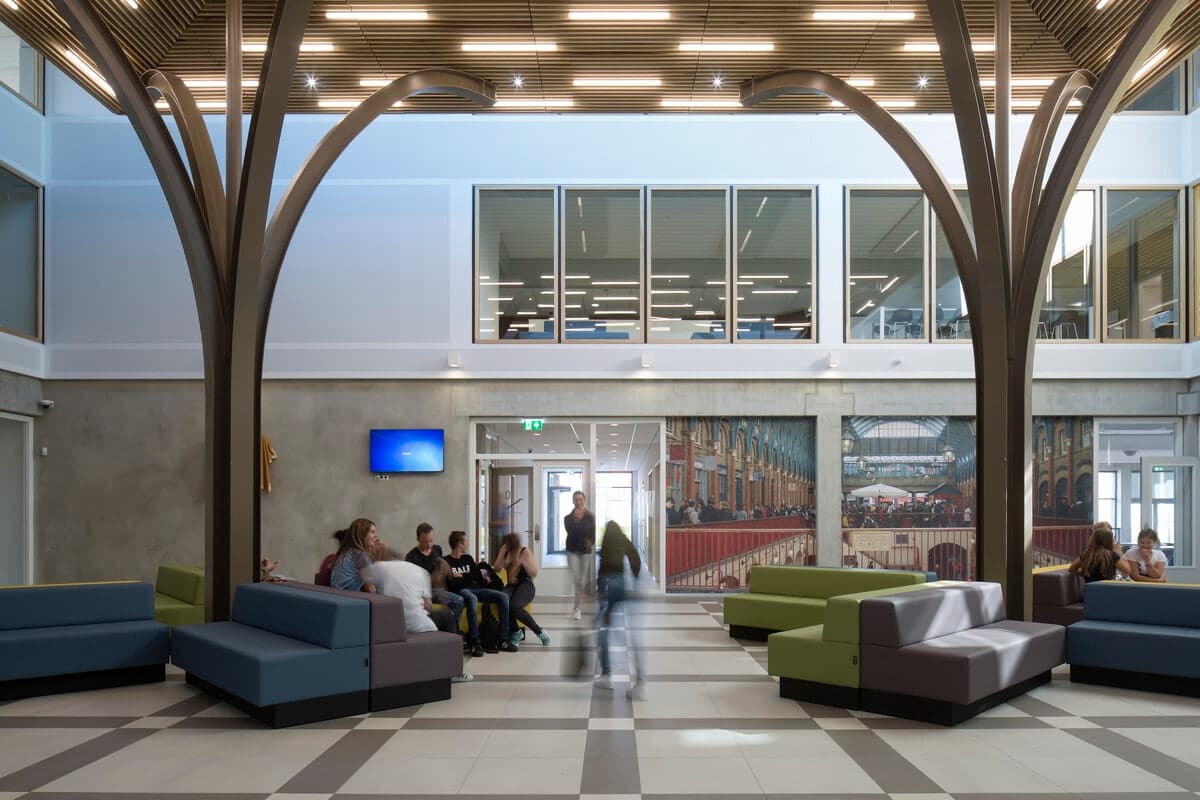 Modern common area with tree-like columns, colourful seating, and high ceilings at VMBO Melanchton Berkroden.